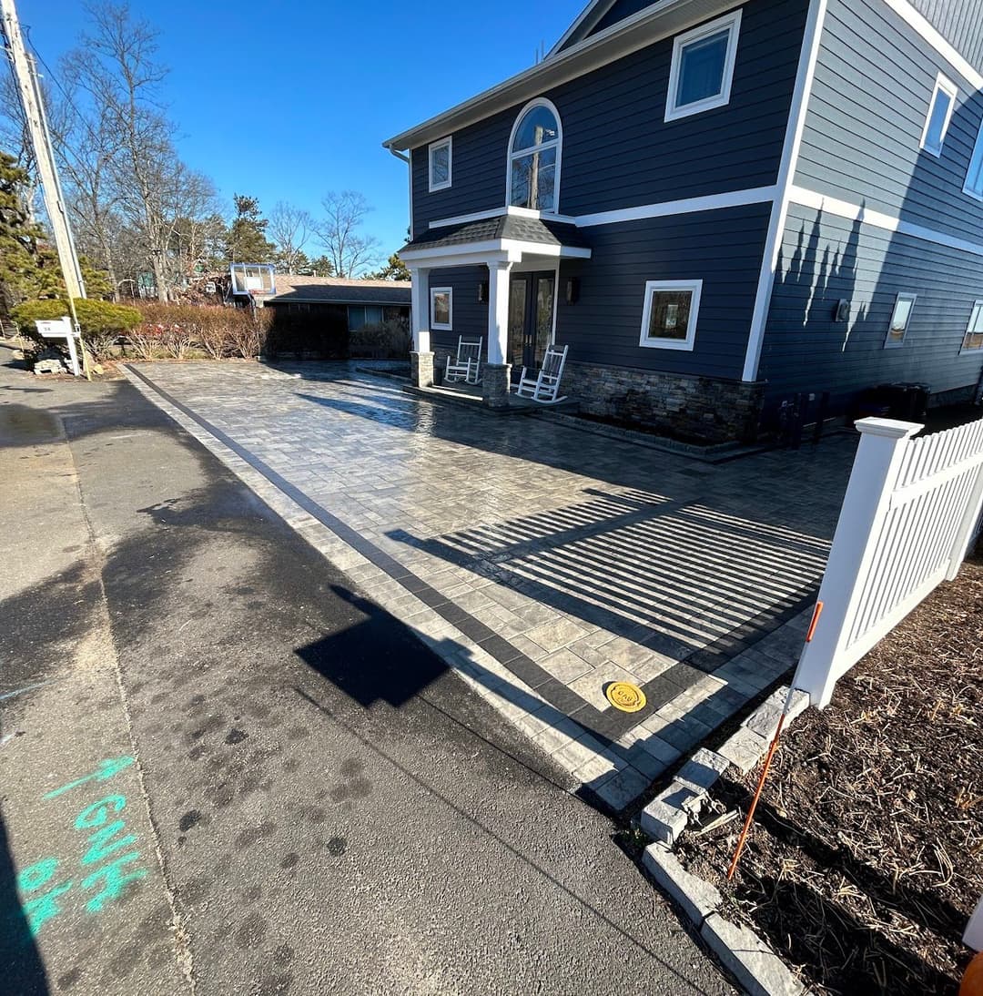 Modern home with gray siding and patterned stone driveway under clear blue sky.