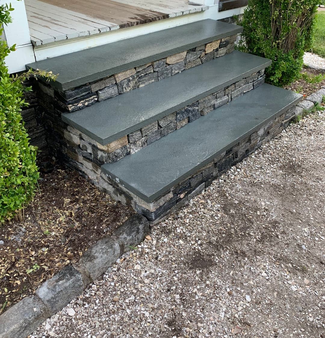 Three-tier stone steps with a gray concrete finish, lined by green shrubs and gravel path.