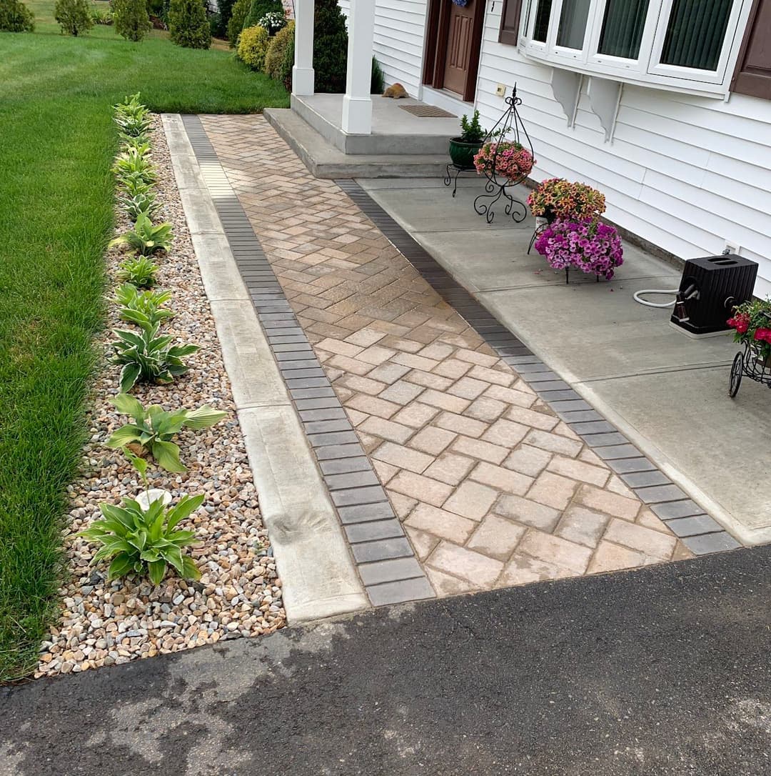Paved walkway with decorative stones and vibrant flower beds enhancing a home's entrance.