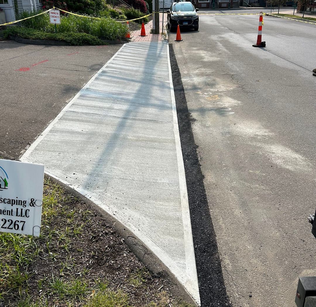 Newly poured concrete curb ramp for improved pedestrian access, with construction signage visible.