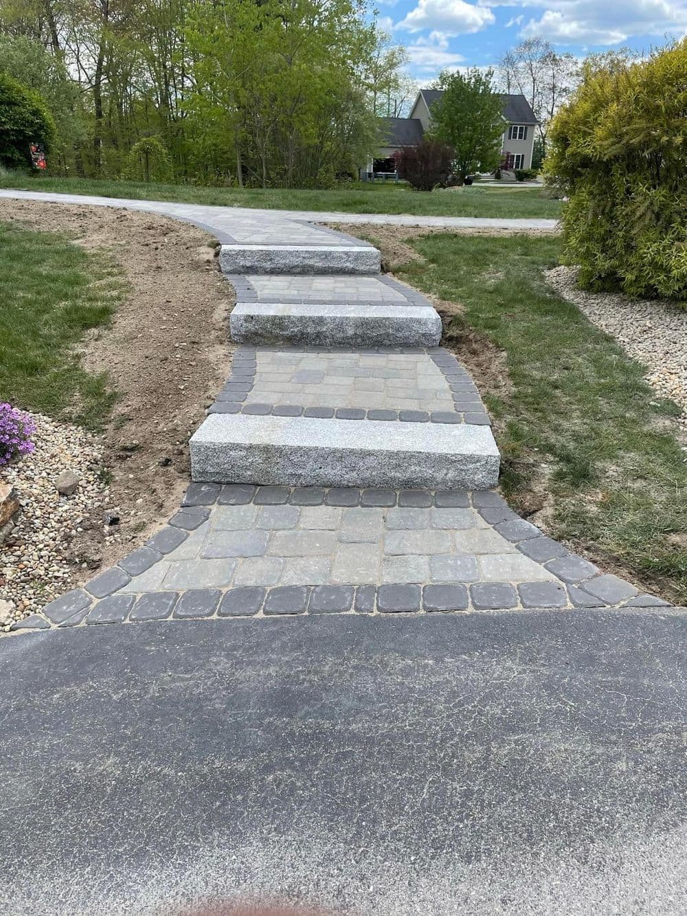 Curved stone pathway leading through a landscaped yard with houses in the background.