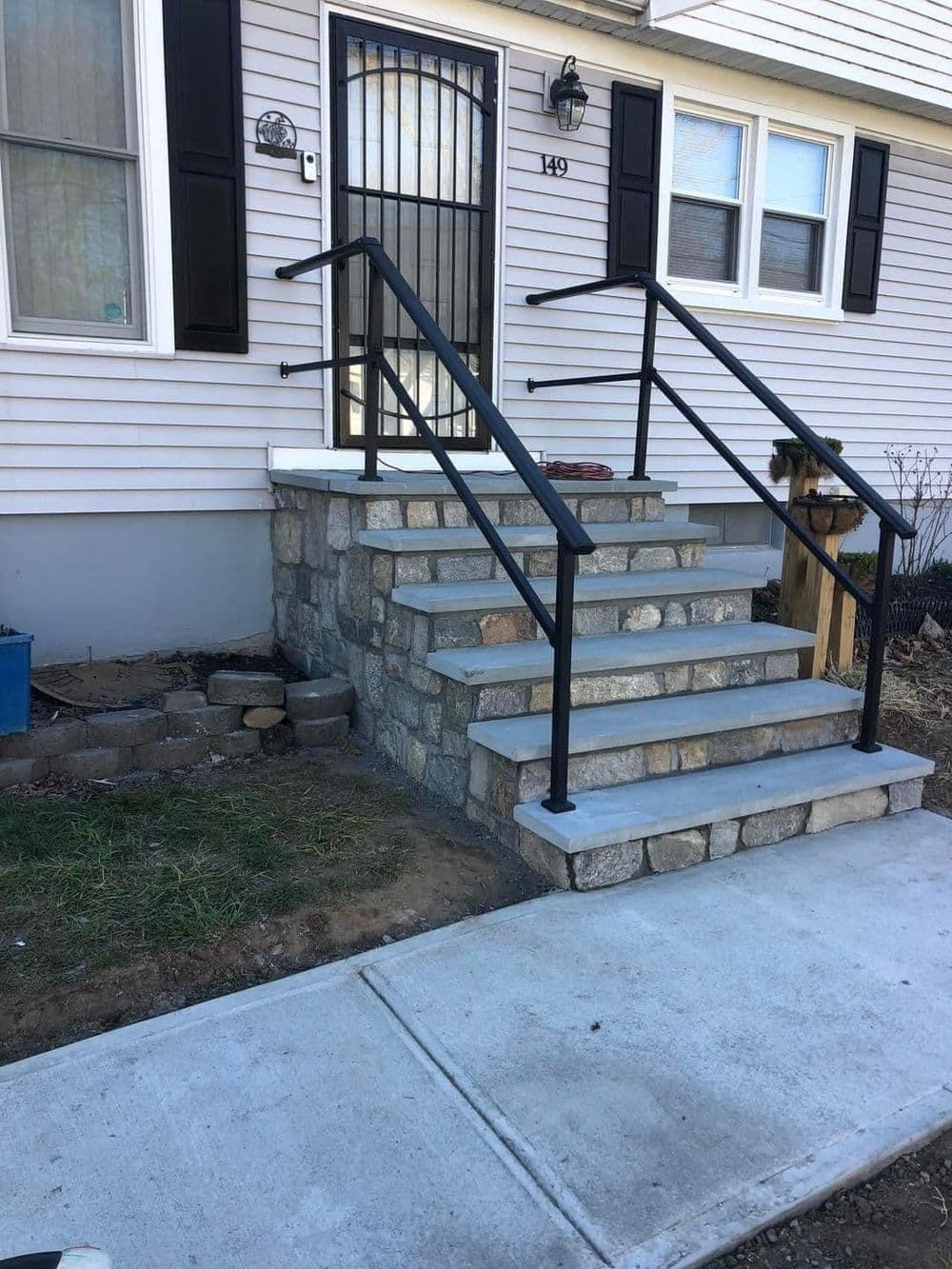 Stone steps with black railings leading to a front door of a house. Round window above.