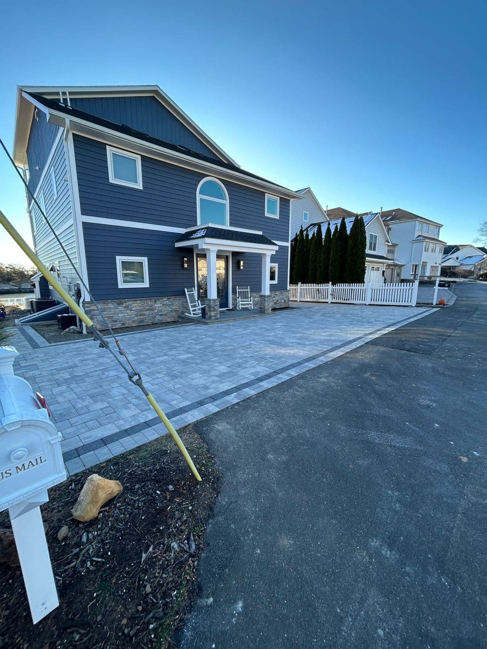 modern blue house with a stone facade and a paved driveway, surrounded by white fence