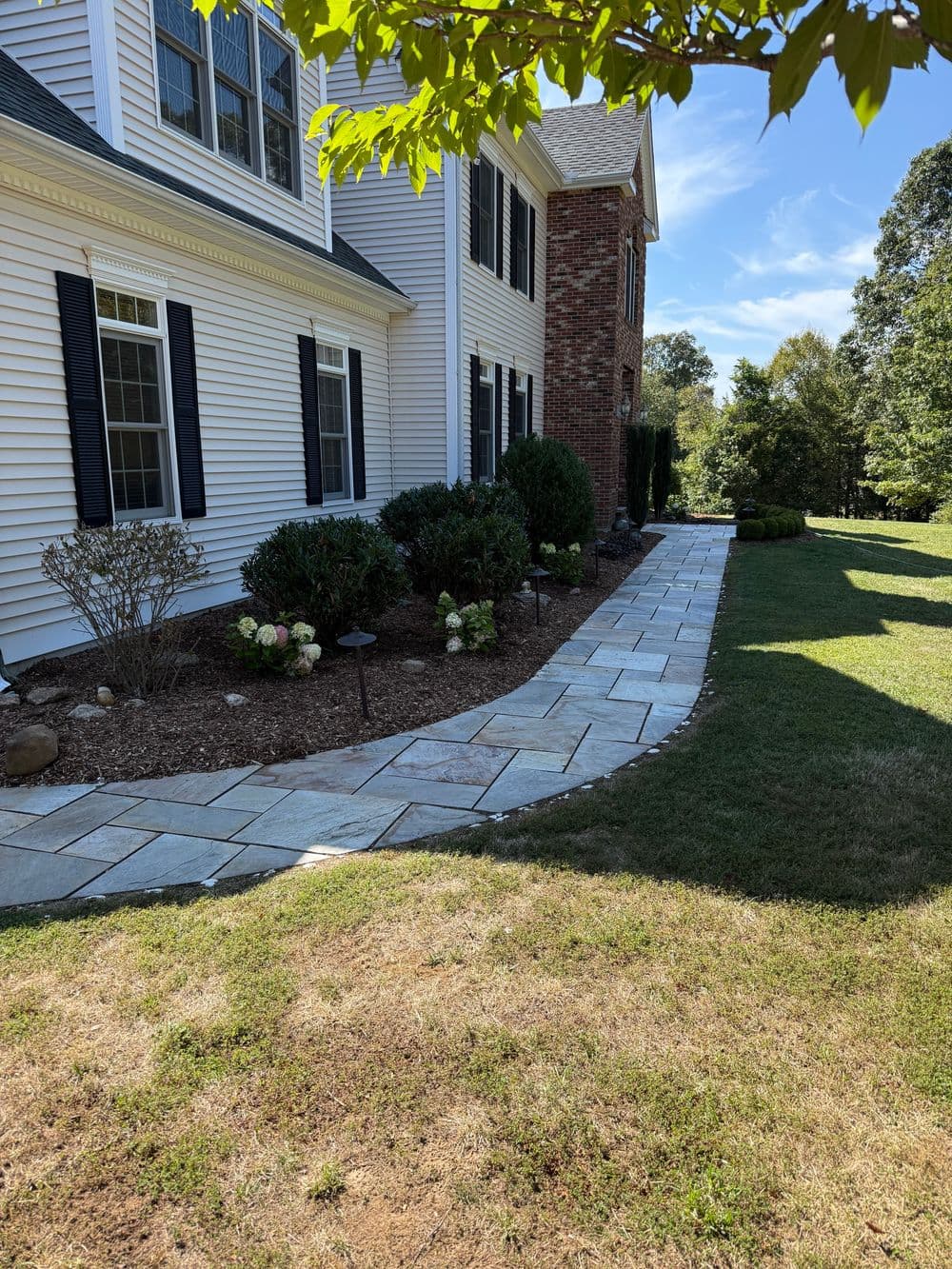 Landscaped pathway with stone pavers, shrubs, and hydrangeas next to a home.