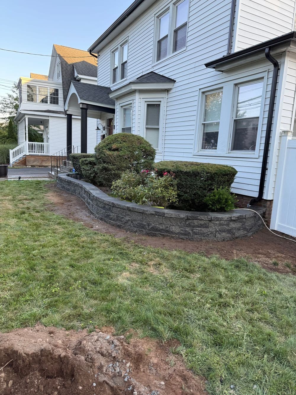 Residential landscaping with stone border and manicured shrubs in front of a white house.