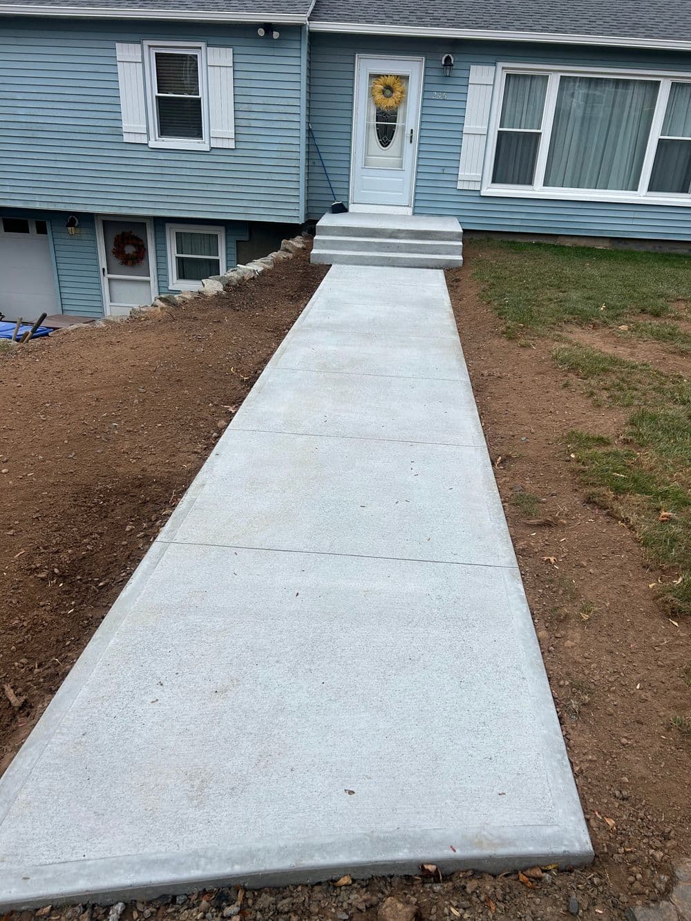 Newly poured concrete walkway leading to a blue house with a front door and sunflowers.