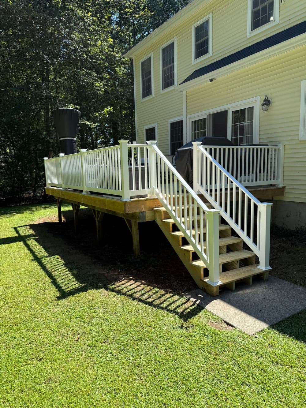 White wooden deck with stairs, surrounded by yard and trees, attached to a yellow house.