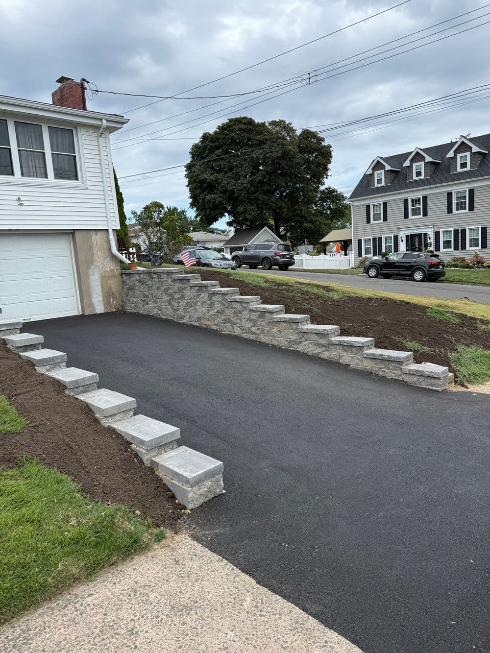 Asphalt driveway with stone steps leading to a house, American flag displayed, suburban setting.